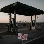 Abandoned electric vehicle charging station standing with moss-covered metal poles and a protest sign reading Justice for EV