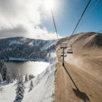 Drone captures contrasting ski resorts with powdery slopes and barren Western terrain illuminated by a sunbeam