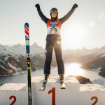 Alice Robinson celebrating a ski jump atop a podium with a gold medal and golden hour light over snow‑covered mountains.