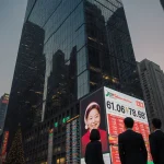 Businesspeople standing near a screen with markets data and reflections in glass skyscraper at dusk with a Christmas Eve glow
