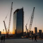 Partially completed high-rise tower looms over Austin skyline at dusk with idle cranes and golden streetlights.