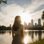 Woman standing on Lady Bird Lake in Austin gazing at sunrise with golden sky reflecting on calm water