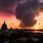 Sunset lights up Austin skyline with Texas Capitol in foreground and dark storm cloud over Lake Travis