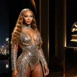 Beyoncé standing confidently on a dimly lit concert stage with gold accents and neon-lit Austin skyline reflected on a Grammy