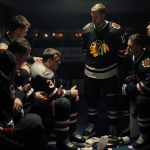Blackhawks players huddle with captain embracing Connor Bedard who wears an ice pack during injury timeout