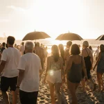 People strolling along Bondi Beach sand with umbrellas and warm golden sunrise light