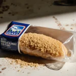 Package of breaded chicken breast revealing soy dust and grains with warm lighting on worn kitchen counter