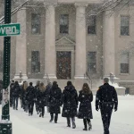 Students walk through snowy campus with Johnson Hall stone façade and police chief standing apart