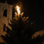 Burning Christmas tree flickers with a single flame and shadows on stone walls of Jenin Holy Redeemer Church