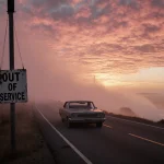 Abandoned car stands on deserted highway with dense fog rolling in and orange pink sunset sky.