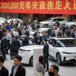 Crowded showroom shows BYD electric cars and luxury models with a banner proclaiming 20,000-yuan subsidy and disappointed Eur
