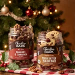 Jars of Choceur holiday bark treats rest on a wooden table with a red tablecloth near a cozy Christmas tree
