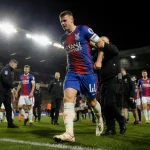 Chris Richards being helped off the pitch with his foot wrapped in bandages and Crystal Palace players showing concern.