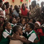 Schoolchildren and teachers hugging family members with festive Christmas decorations and warm light in Nigeria