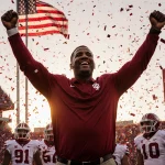 Coach Bryant Haines raising his arms with confetti falling and an Indiana flag in the sunset stadium