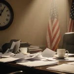 Cluttered congressional desk scattered with papers and coffee cups with a 11:59 clock and a fading flag.