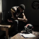 Damon Wilson II sits with hands looking down with a crumpled NIL agreement in front and a Georgia Bulldogs logo behind