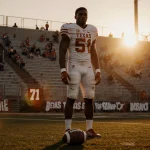DeAndre Moore Jr., Texas Longhorns, stands alone on the football field at night with a worn ball near his feet and bleachers