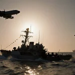 Destroyed boat floats on waves with a sun dipping in western sky and a U.S. aircraft shadow overhead