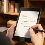 Person holding sleek digital notebook with warm wooden background and soft side light.