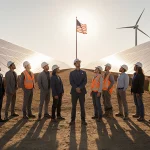 Diverse clean energy professionals standing together with solar farm and waving American flag behind.
