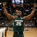 Divine Ugochukwu raises arms in celebration with confetti raining and scoreboard reading 76-72