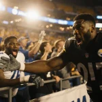 DK Metcalf reaches a fan’s arm with a shocked expression and stadium lights casting a harsh shadow.