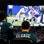 A lone fan bowing with eyes on Jumbotron split-screen showing incomplete conversion with bright Eagles logo on scoreboard