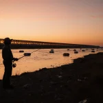 Environmentalist standing with a fishing rod near Rio Grande where buoys float and microplastics swirl in the water.