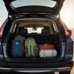 Honda CR‑V unfolds cargo space with luggage and mountain backdrop in natural light and warm glow
