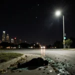 Dark shape lies on ground after fatal collision with scattered leaves and shattered glass illuminated by car headlights near