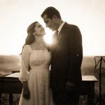 Abraham Quintanilla stands proudly beside Selena smiling with a worn wooden table behind them