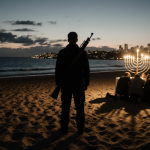 Lone figure standing at Bondi Beach dusk with rifle hint and shocked Hanukkah crowd behind golden light casting long shadows