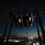 Two riders hanging midair on Circuit Breaker roller coaster at COTA with tense faces and long shadows in dark night sky.