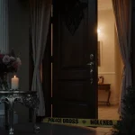 Open front door reveals dim hallway with candle and police tape.