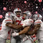 Buckeyes players hugging each other with confetti falling and stadium lights glowing behind them
