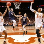 Kyla Oldacre leaps for a slam dunk with Madison Booker high‑fives and the Texas Longhorns logo glowing above.