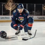 Matthew Tkachuk lacing up his Panthers hockey skates with focused expression and Winter Classic lights.