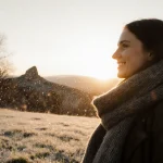 Woman wrapping scarf around neck smiling with winter morning grass and sunrise behind bare trees in Austin Hill Country