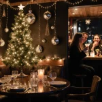 Patrons laugh while sipping cocktails with a Christmas tree and disco balls reflected on glassware