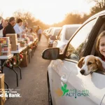 Volunteer handing out groceries and pet supplies with smiling drivers and a child clutching a stuffed animal.