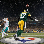 Aaron Rodgers passing a touchdown to DK Metcalf with green jersey under falling snow in night game