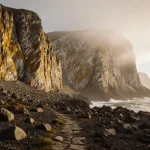Granite quarry cliffs towering with weathered gold and white patterns under soft diffused light beside misty Scottish coastli