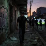 Mario Pineida stands near graffiti wall in Guayaquil with shattered glass and watching broken screens.