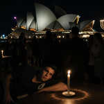 Medical team rushing to help young man lying on ground with Hanukkah candle glow and Sydney Opera House silhouette behind.