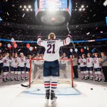 Hilary Knight raising her stick high with jersey number 21 and scoreboard showing 4-1