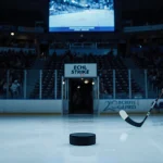 Hockey puck lying abandoned on ice with chairs and lone stick leaning against the wall in an arena showing a strike.