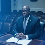 Speaker Mike Johnson stands at podium with healthcare plan document and empty chairs in dim chamber political tension