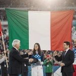 President Sergio Mattarella presenting flags to athletes with Italian Olympic flag behind and cheering crowd