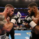Jake Paul jabs at Anthony Joshua with sweat and intense stare amid bright boxing lights in Miami.